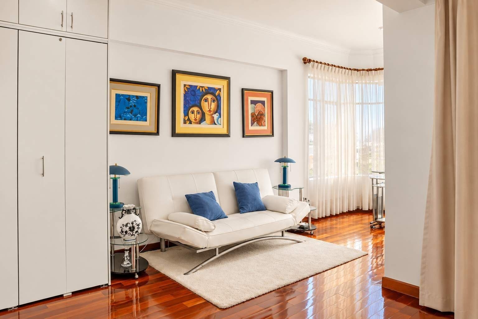 A modern living room with a white sofa, blue cushions, and three framed artworks on the wall.