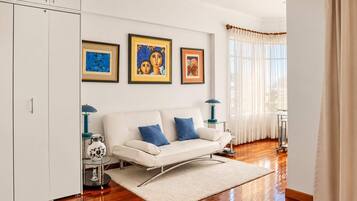 A modern living room with a white sofa, blue cushions, and three framed artworks on the wall.