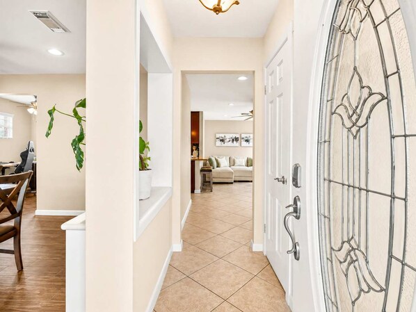 A hallway with a dining area, a living room, and a door with a decorative glass panel. - 2BR with Movie Room I Pool I Easy Access to NRG (Houston)