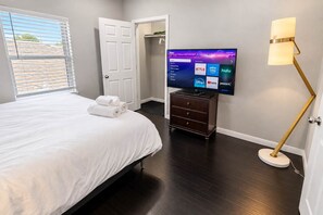 Une chambre d’hôtel avec un lit, un téléviseur posé sur un meuble, une lampe et une porte donnant sur une autre pièce.