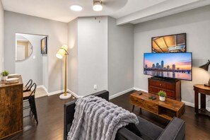 A modern living room with a flat-screen TV mounted on the wall, a wooden coffee table, a grey sofa, and a floor lamp. - FIFA Stay 2BR Near NRG  DT   Med Center -4 (Houston)