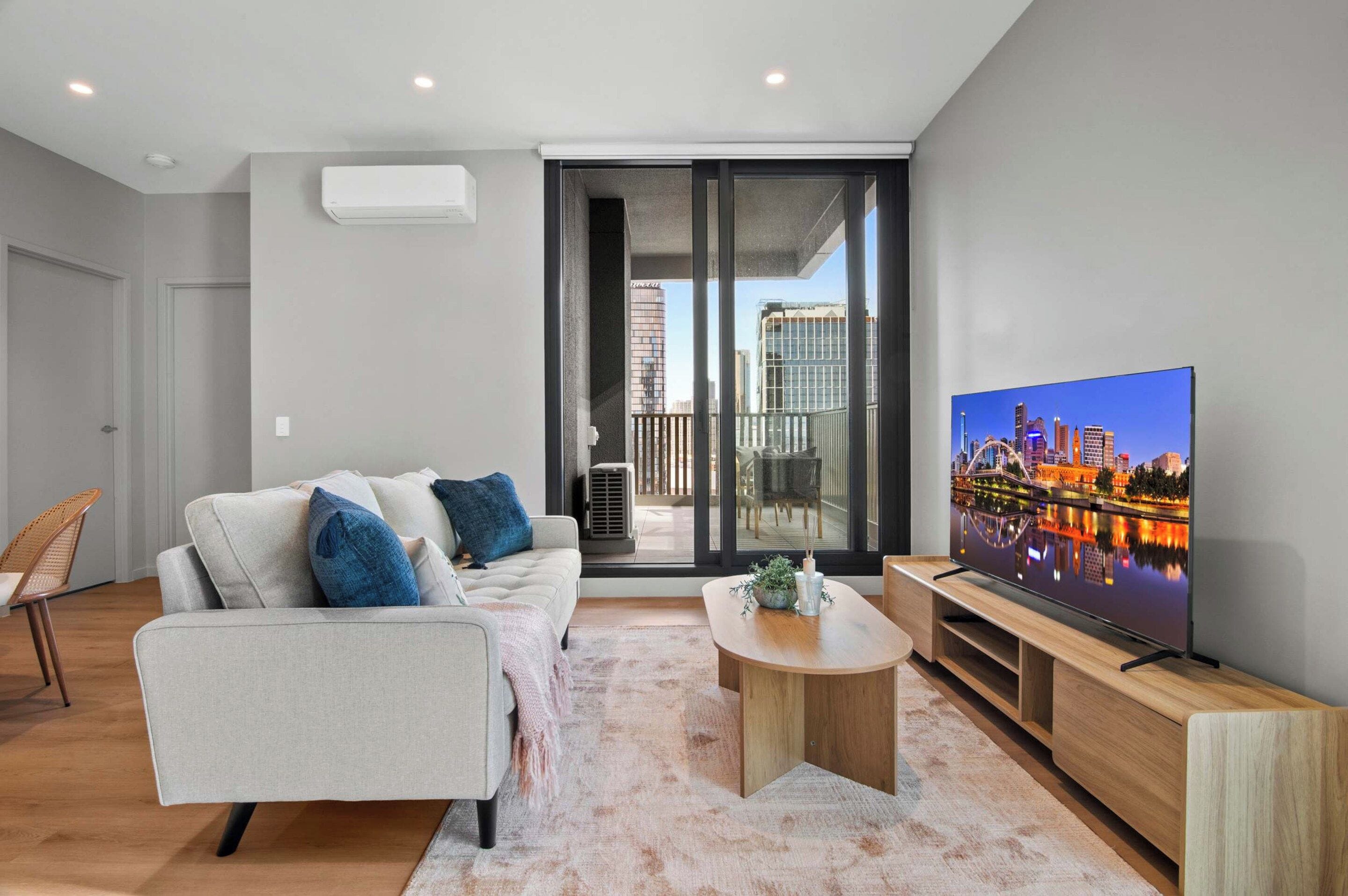 A modern living room with a sofa, a coffee table, a TV, and a balcony with a city view.