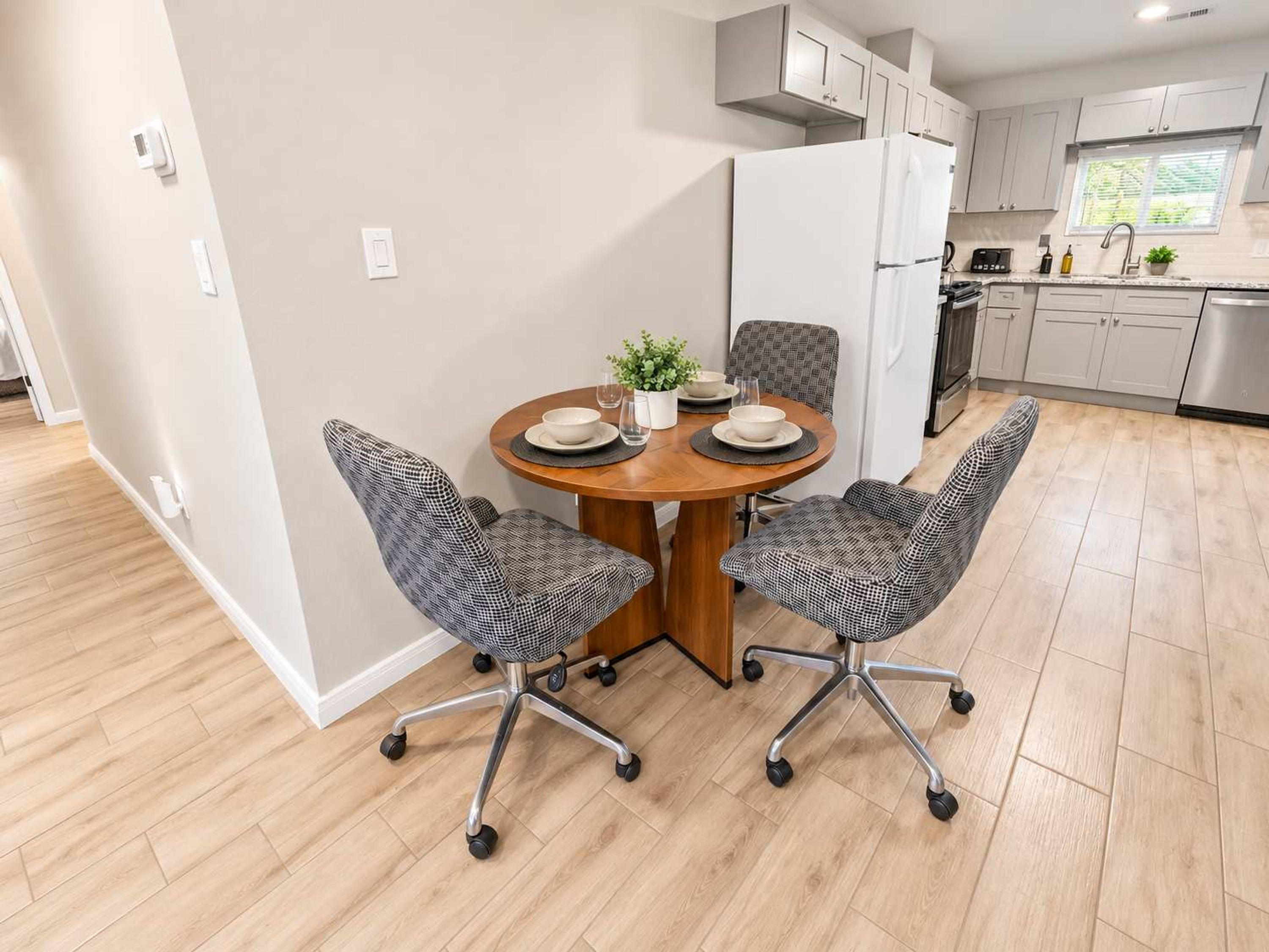 A modern kitchen with white cabinets, a stainless steel refrigerator, and a dining area with a round wooden table and patterned chairs.