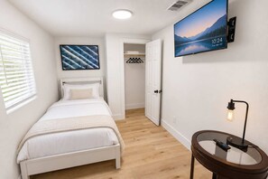 A bedroom with a bed, a TV mounted on the wall, a bedside table with a lamp, and a window with blinds. - FIFA 2 Apt Bundle Near NRG  DT   Med Center - 12 (Houston)