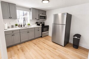 Eine moderne Küche mit grauen Schränken, Edelstahlgeräten, einer weißen Arbeitsplatte und einem Holzboden.