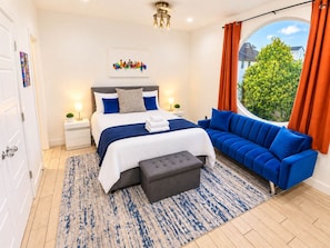 A modern bedroom with a large bed, a blue sofa, a small table, and a window with curtains. - Montrose Rooftop Townhome   3 Suites  Sleeps 8 (Houston)