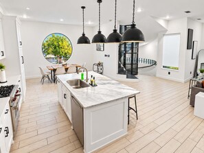 A modern kitchen with a central island, pendant lighting, and a view of the outdoors. - Montrose Rooftop Townhome   3 Suites  Sleeps 8 (Houston)