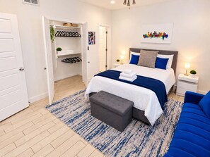 A modern bedroom with a bed, bedside tables, a bench, a wardrobe, and a colorful artwork on the wall. - Montrose Rooftop Townhome   3 Suites  Sleeps 8 (Houston)