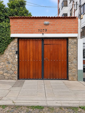 A double wooden garage door with a number '7079' above it, set against a stone wall with a tiled roof. - Walk to Telef  rico and Megacenter I 2BR I Parking (La Paz)