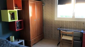 A room with a bed, a desk with a chair, a wardrobe, and a window.