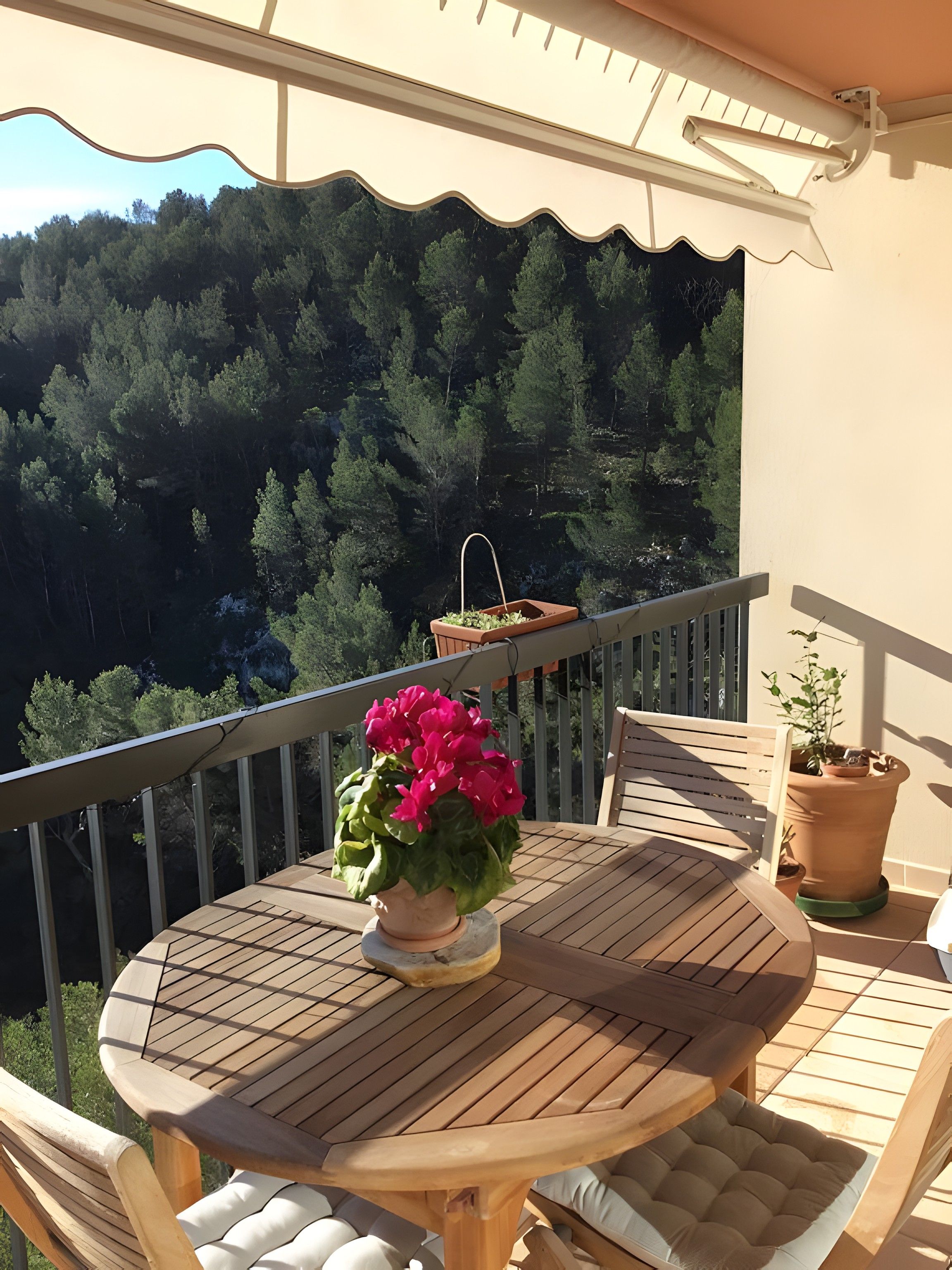 A wooden table and chairs on a balcony with a view of a forested hillside.