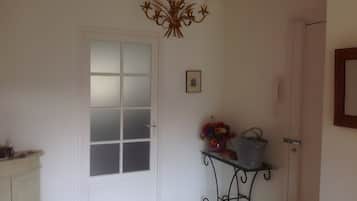 A room with a white door, a chandelier, a framed picture, and a small table with a basket.