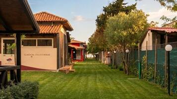Un sentiero conduce a una casa italiana in stile classico, con tetto in tegole rosse, circondata da vegetazione e un recinto.