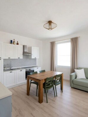 A modern kitchen with white cabinets, a wooden dining table, and a green sofa.