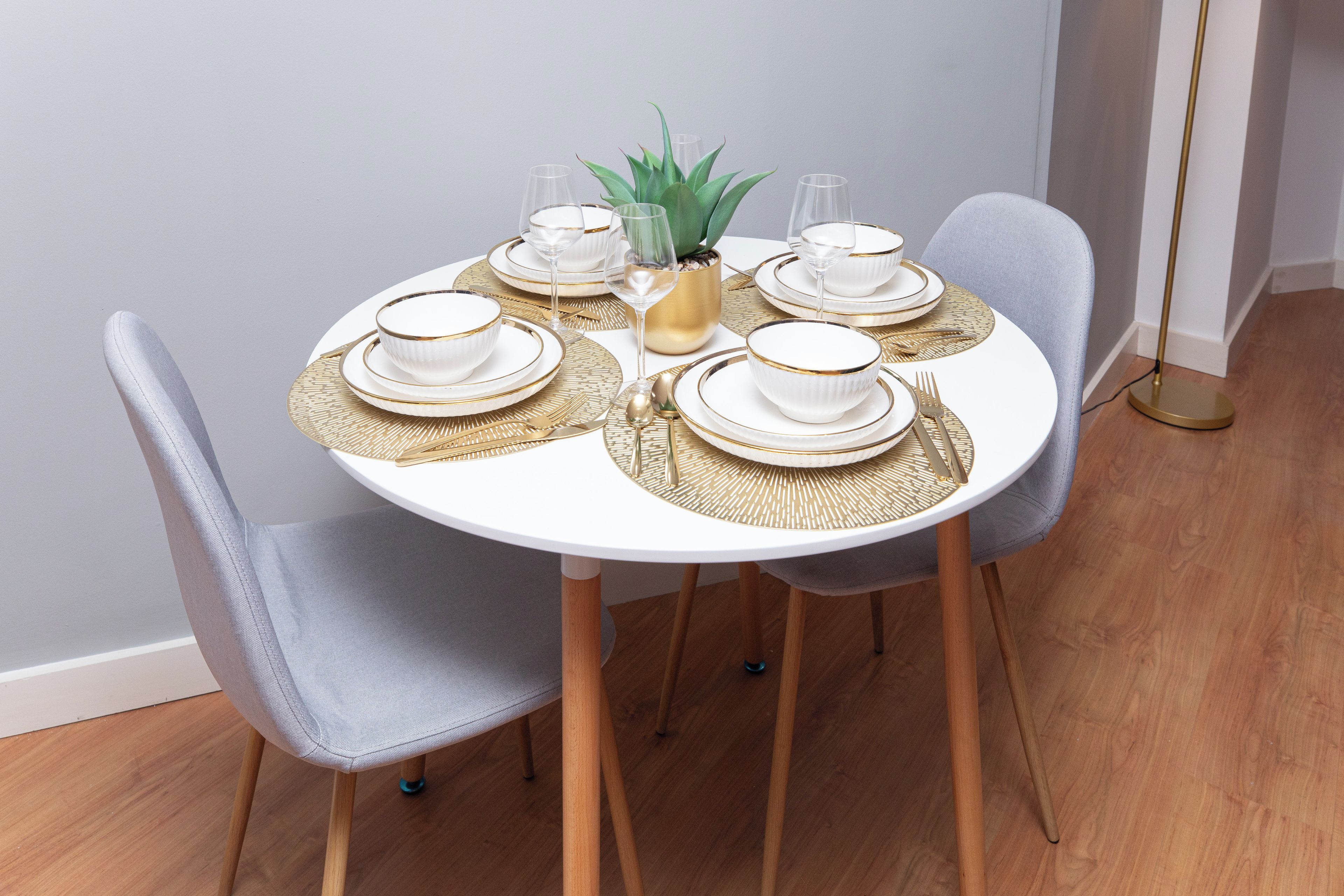 A round dining table set with white plates, gold-rimmed bowls, and gold cutlery.