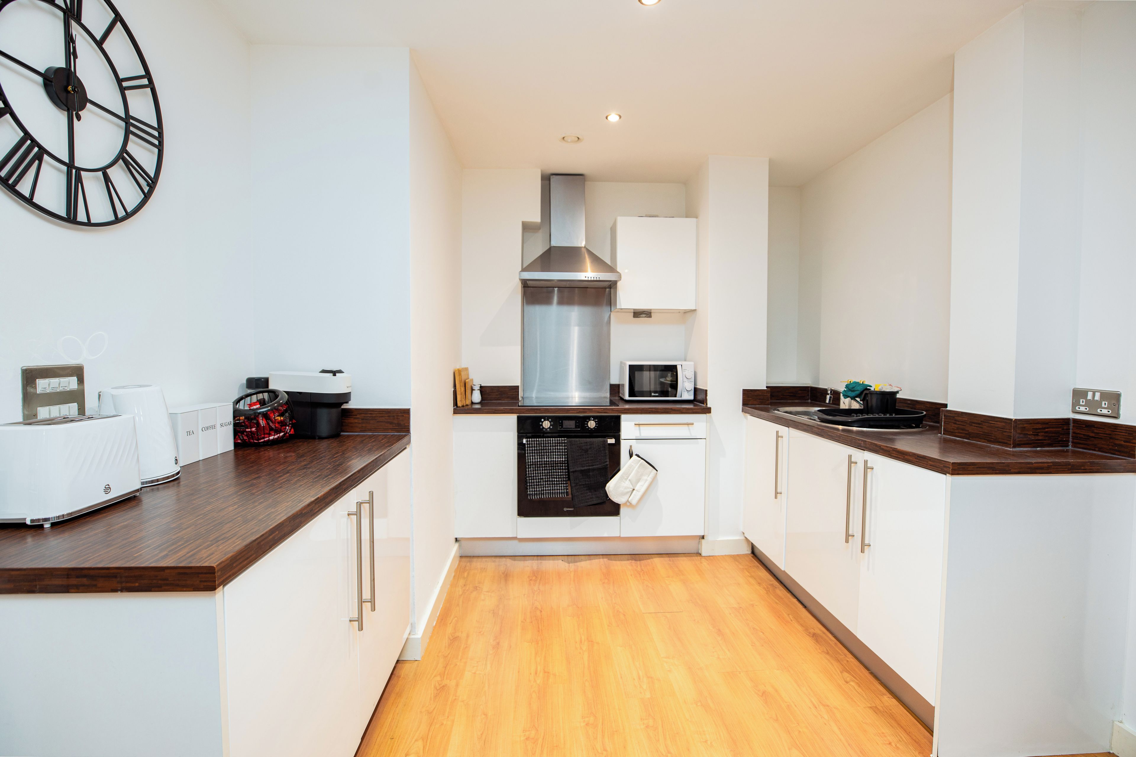 A modern kitchen with white cabinetry, a stainless steel range hood, a microwave, and a clock on the wall.