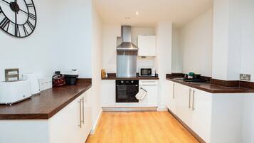 A modern kitchen with white cabinetry, a stainless steel range hood, a microwave, and a clock on the wall.