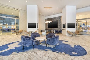 Un vestíbulo moderno con suelo de mármol, zona de estar con sofás y sillones, y una pantalla de televisión grande.