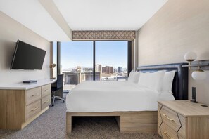 Habitación de hotel con una cama grande, un escritorio, un televisor y vistas a la ciudad.