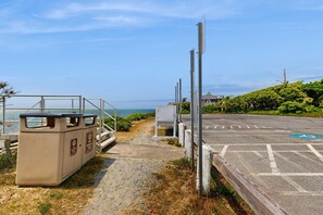 A parking area with a clear view of the sea, a trash bin, and a pedestrian crossing. - Adorable Cottage With Patio & Walk to Sea St Beach (Dennis)