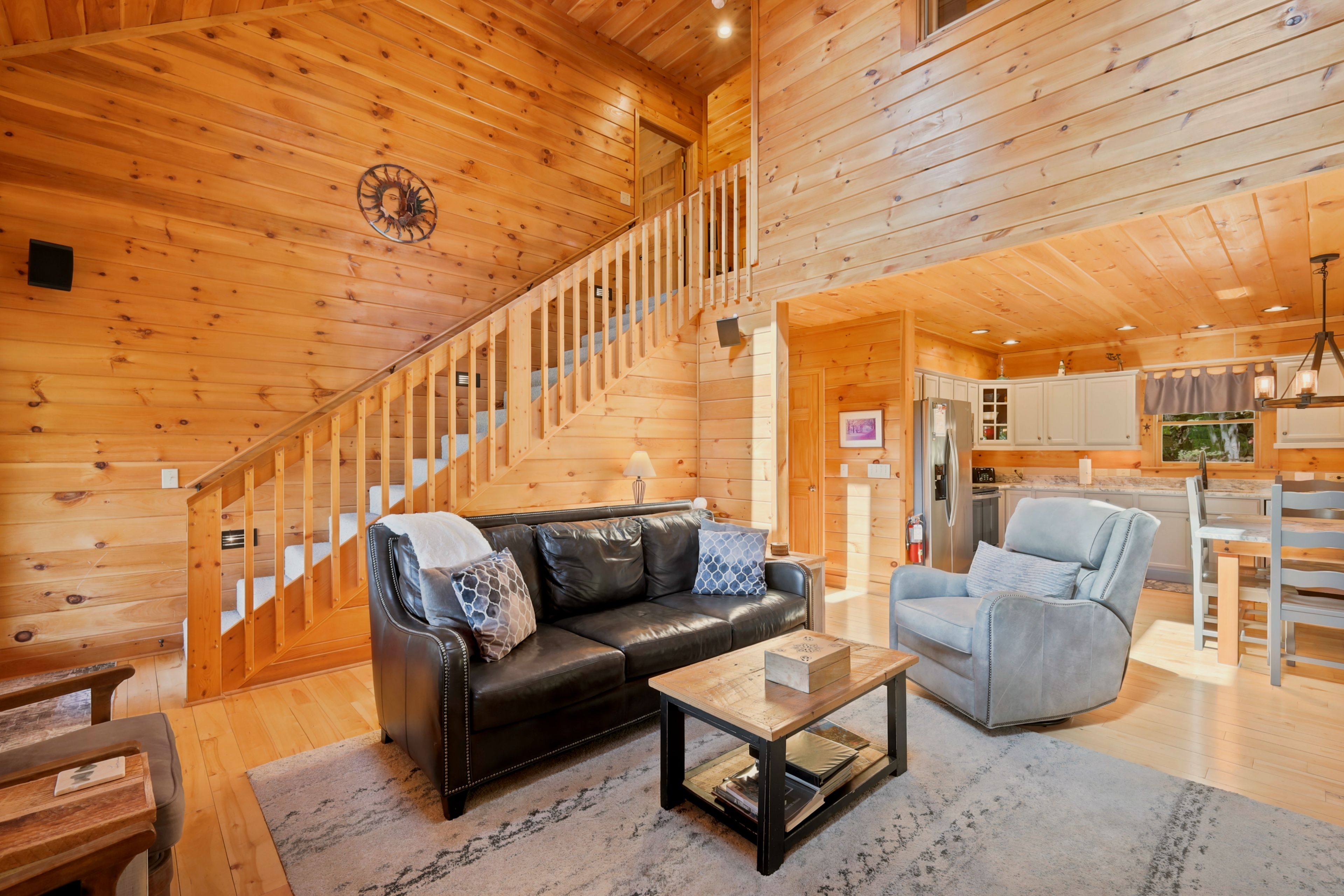 A wooden interior with a staircase, a leather sofa, a blue armchair, and a kitchen area.
