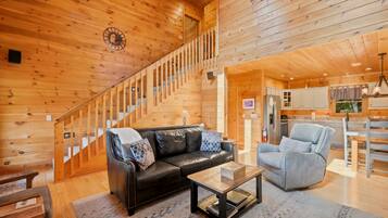 A wooden interior with a staircase, a leather sofa, a blue armchair, and a kitchen area.