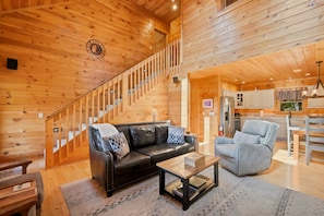 A wooden interior with a staircase, a leather sofa, a blue armchair, and a kitchen area.