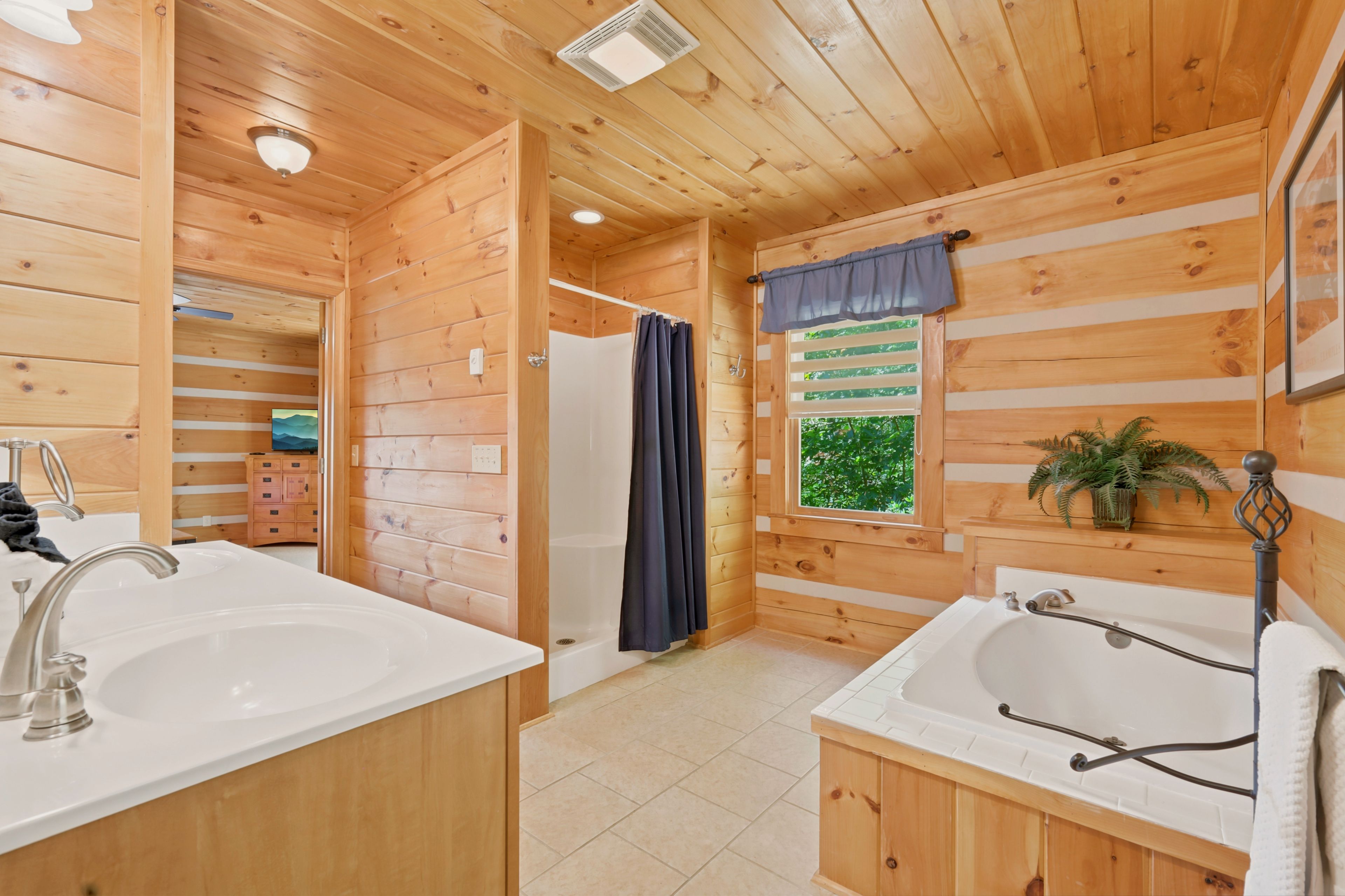 A wooden cabin bathroom with a shower, two sinks, and a window with a view of greenery.