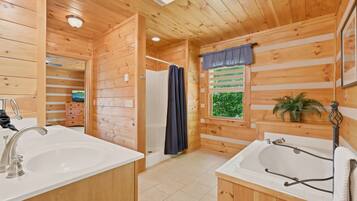 A wooden cabin bathroom with a shower, two sinks, and a window with a view of greenery.