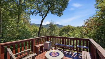 Une terrasse dotée d’un foyer extérieur, de sièges et offrant une vue sur une chaîne de montagnes boisées.