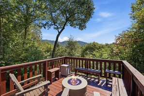 A deck with a fire pit, seating, and a view of a forested mountain range.