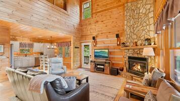 A log cabin interior with a fireplace, seating area, kitchen, and stone wall.
