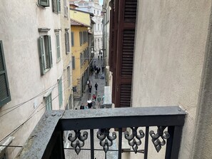 Un carrer estret amb edificis a ambdós costats, una barana metàl·lica al primer pla i persones caminant pel carrer.