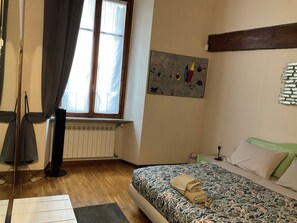 A bedroom with a bed, a radiator, a window with curtains, a painting on the wall, and a bedside table. - BERGAMO ALTA SUITE - Spacious apartment in the heart of Bergamo Alta (Bergamo)
