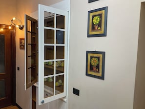 A hallway with a white door, a lit wall lamp, and two framed artworks on the wall. - BERGAMO ALTA SUITE - Spacious apartment in the heart of Bergamo Alta   (Bergamo)