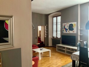 Un saló amb un sofà blanc, una butaca vermella, una taula de centre blanca i un moble per a la televisió.