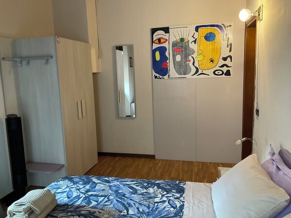 Un dormitori amb llit, armari, mirall i una paret amb obra d'art abstracta.