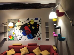 A room with a red sofa, a colorful abstract painting on the wall, and multiple hanging lamps. - BERGAMO ALTA SUITE - Spacious apartment in the heart of Bergamo Alta (Bergamo)