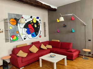 Un salon moderne avec un canapé d’angle rouge, une table basse blanche et un tableau abstrait aux couleurs vives accroché au mur.