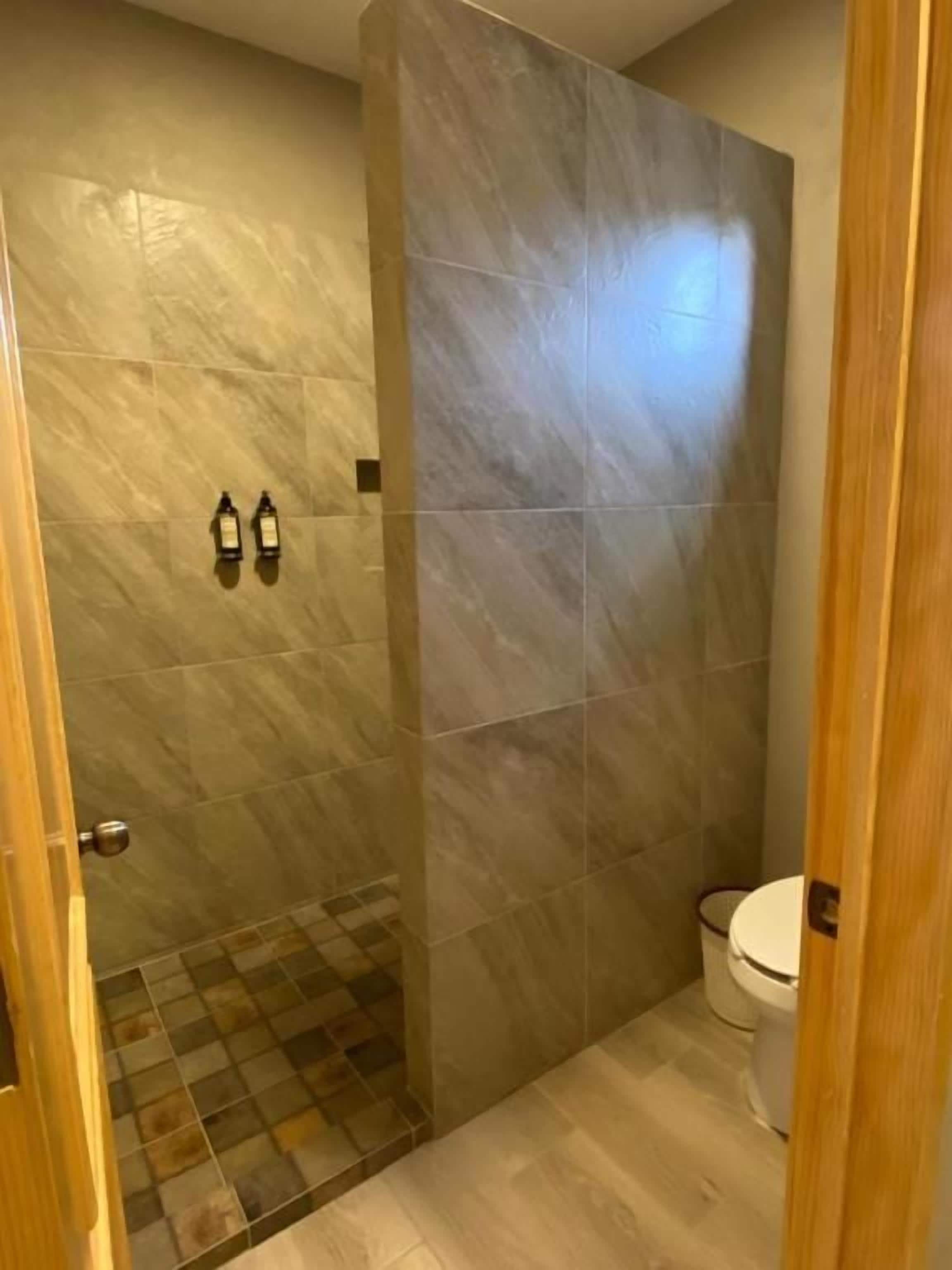 A bathroom with a shower area, a toilet, and a tiled floor.