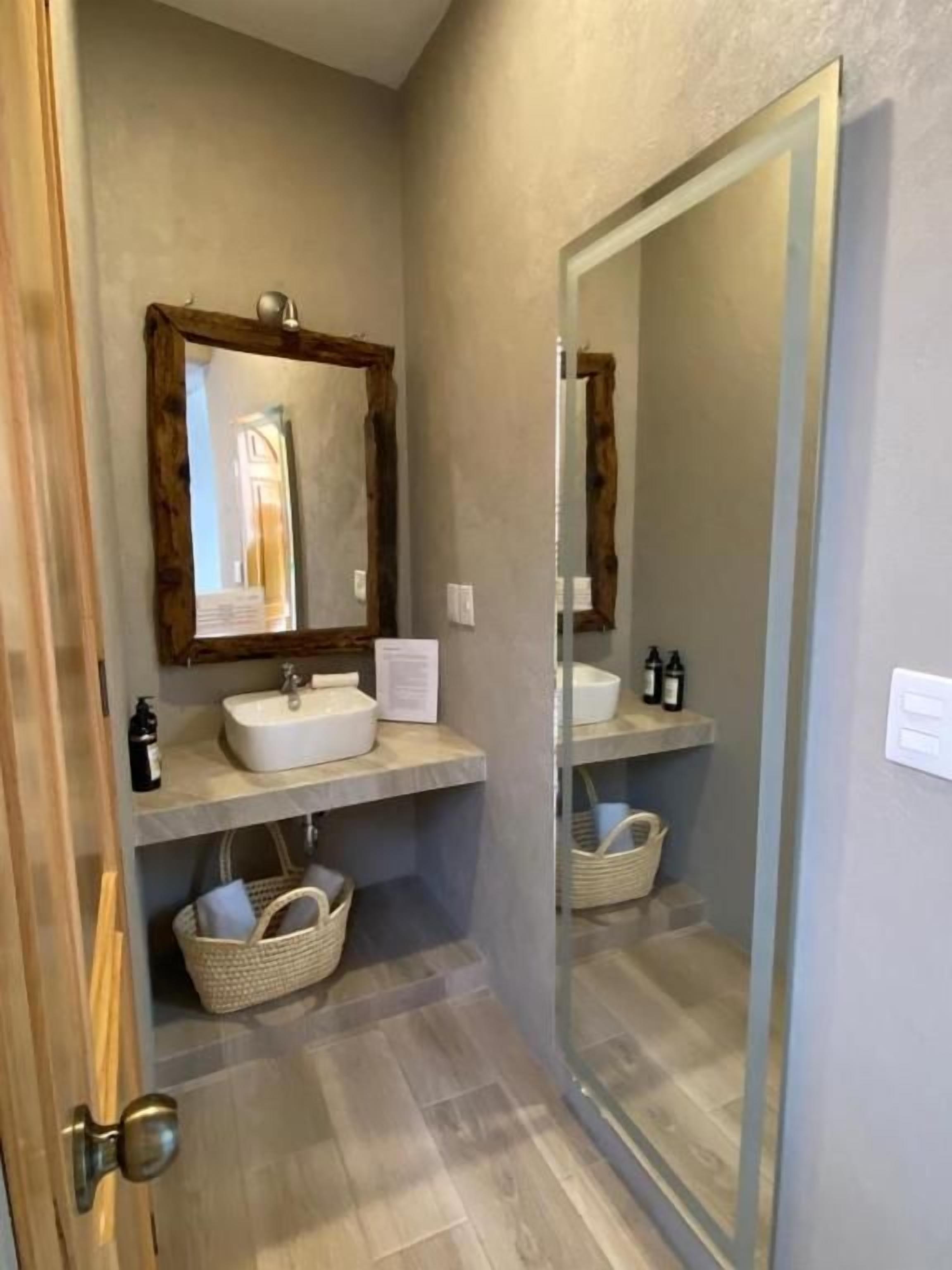 A bathroom with a wooden-framed mirror, a white sink, and a shelf with toiletries.