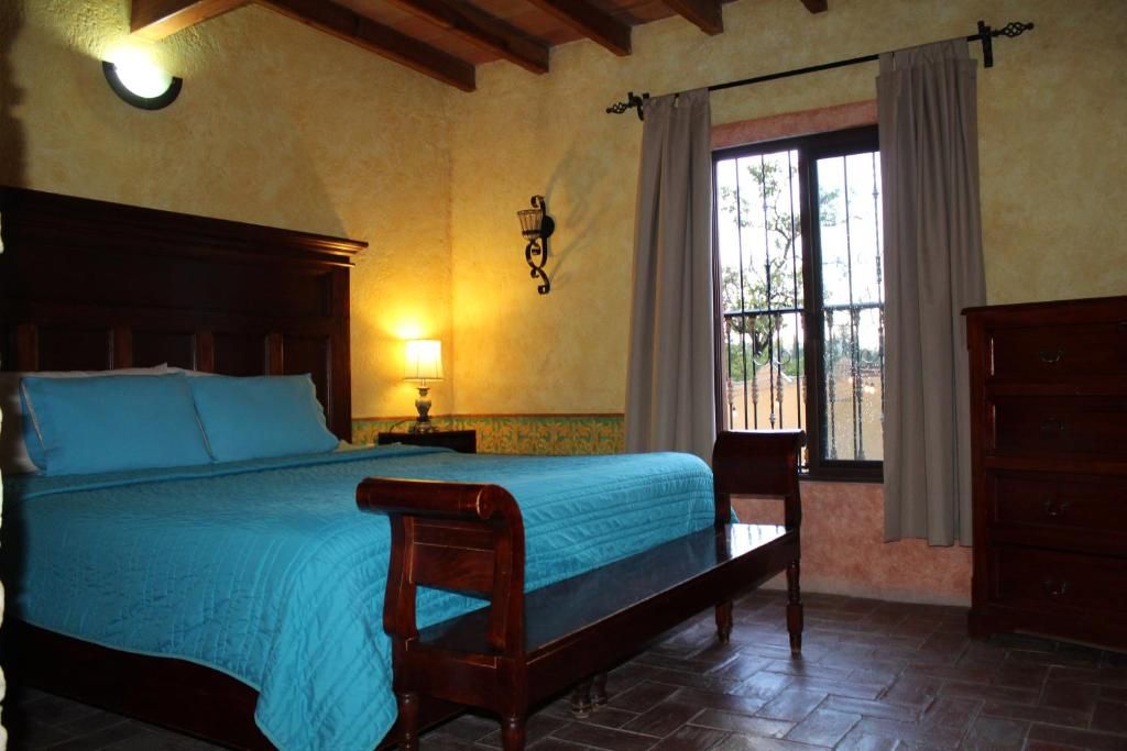 Un dormitorio con cama, mesita de noche, lámpara, ventana con cortinas y cómoda de madera.