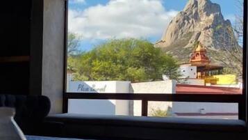 A hotel room with a large window, a bed, a table, and a bottle of water.