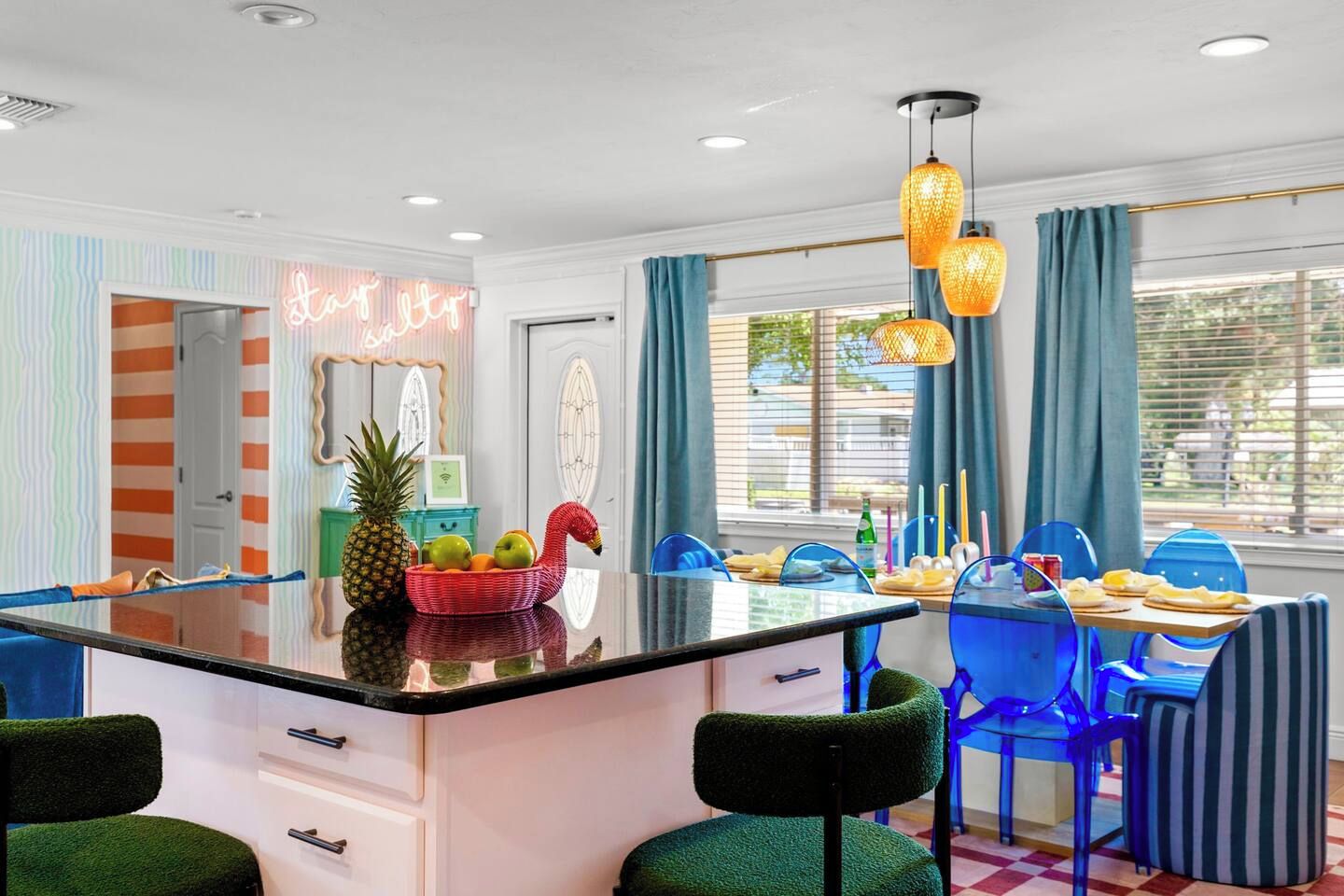 A kitchen with a central island, blue chairs, and a neon sign.