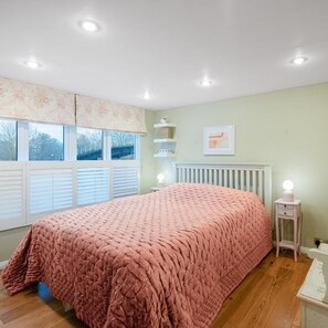 Ein Schlafzimmer mit einem großen Bett, einem Heizkörper, einem Nachttisch mit Lampe und einem Fenster mit Jalousien.