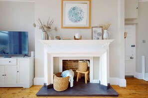 A room with a white fireplace, a television on a cabinet, and a framed artwork above the mantel. - Serene 2BR near Putney Heath and Wimbledon area (London)