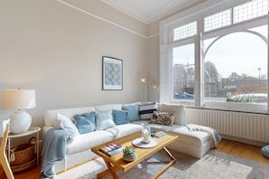 Un salon avec un canapé blanc, une table basse en bois, une lampe et un tableau encadré au mur.