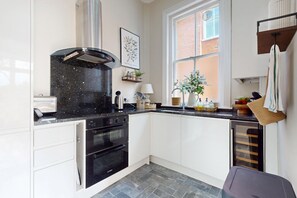A compact kitchen with a Bosch oven, a black range hood, a window with a view of a brick building, and a hanging towel rack. - Serene 2BR near Putney Heath and Wimbledon area (London)