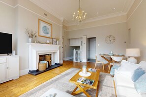 A living room with a fireplace, a television, a dining area with a table and chairs, and a kitchen in the background. - Serene 2BR near Putney Heath and Wimbledon area (London)