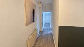 A narrow hallway with a radiator, a door at the end, and a light fixture. - East London Compact Bedroom, Sleeps 1 With Wifi (London)